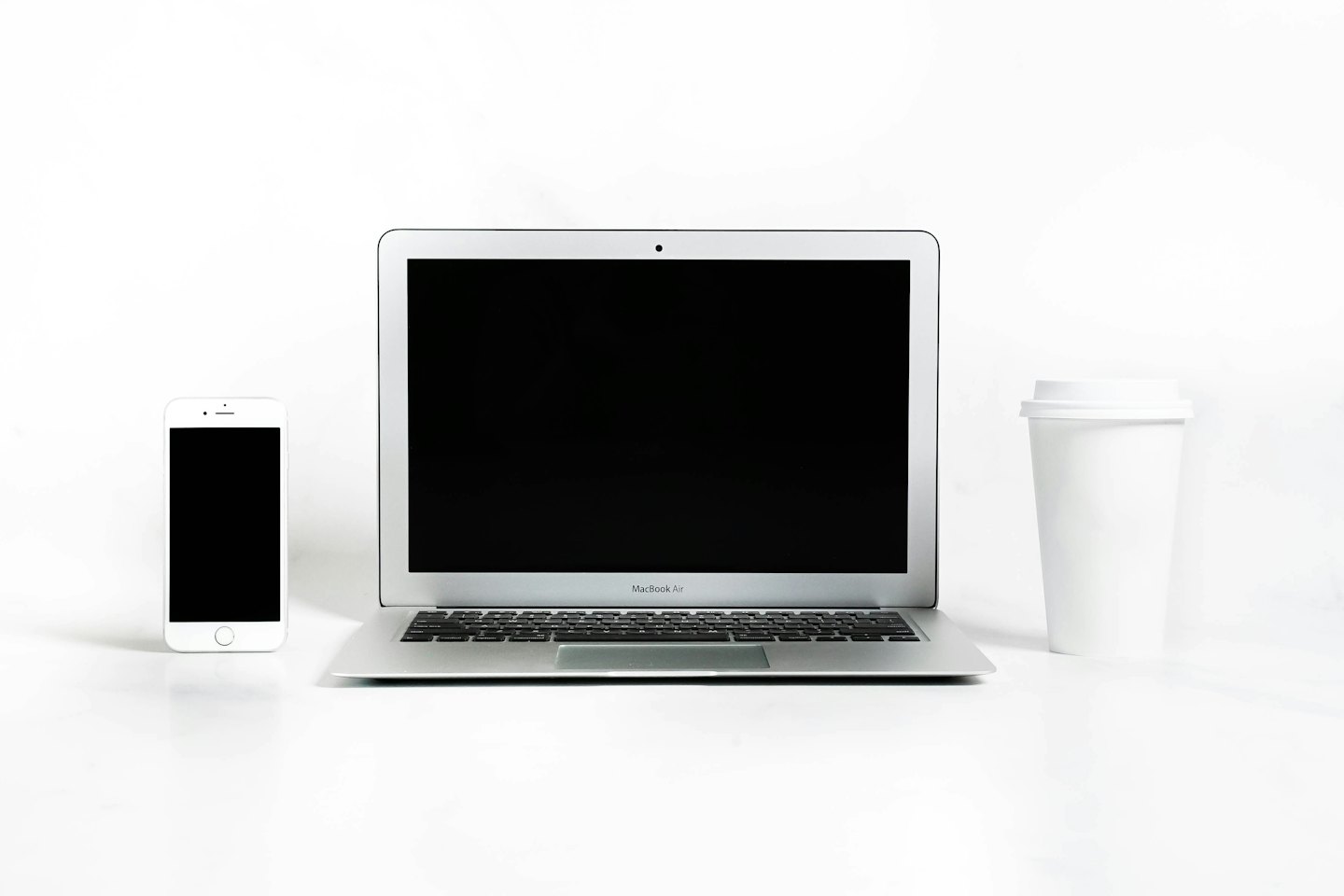 Laptop, smartfon i kubek kawy na białym biurku.